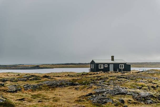 uma pequena casa em uma colina rochosa com vista para um corpo de água - Foto, Imagem