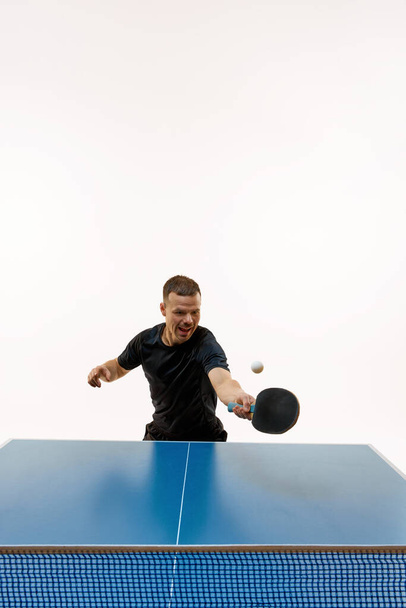 Siyah spor üniformalı masa tenisçisi, beyaz stüdyo arka planına karşı yoğun bir şekilde topa vuruyor. Uzayı kopyala Profesyonel spor, dinamik ve enerji kavramı, şampiyonluk, turnuva. Ad. - Fotoğraf, Görsel