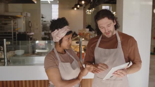 Jovens trabalhadores de padaria masculinos e femininos vestindo aventais em pé no café, olhando para a tela do tablet digital e tendo discussão durante o dia de trabalho - Filmagem, Vídeo