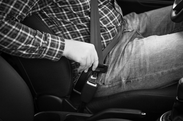 Black and white closeup of man fastening seat belt in car - 写真・画像