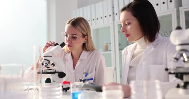 Zwei erfolgreiche Chemiker, die im Labor arbeiten, untersuchen Experimente unter dem Mikroskop und halten die Daumen hoch. Erfolgreiches chemisch-medizinisches Experiment im Labor - Filmmaterial, Video