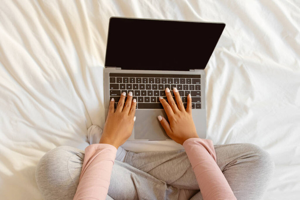 Неузнаваемая черная беременная женщина с ноутбуком с пустым пустым экраном, сидя на кровати у себя дома, вид сверху Снимок ожидаемой матери покупки в Интернете или работы удаленно, макет - Фото, изображение