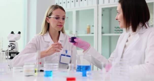 Kosmetyczny chemik i kolega wącha niebiesko-fioletową substancję płynną z kolby szklanej i przeprowadza eksperymenty w laboratorium. Testowanie produktów kosmetycznych w laboratorium - Materiał filmowy, wideo