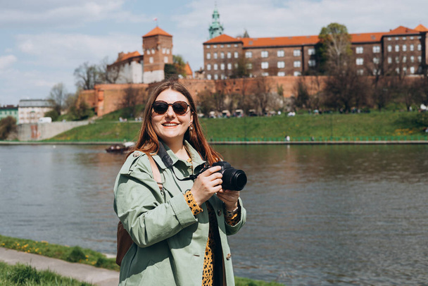 クラクフの有名なワイエル城でカメラで写真を撮るスタイリッシュな服で30人の女性観光客. 魅力的な若い女性観光客が新しい街を探索しています. 春にヨーロッパを旅する - 写真・画像