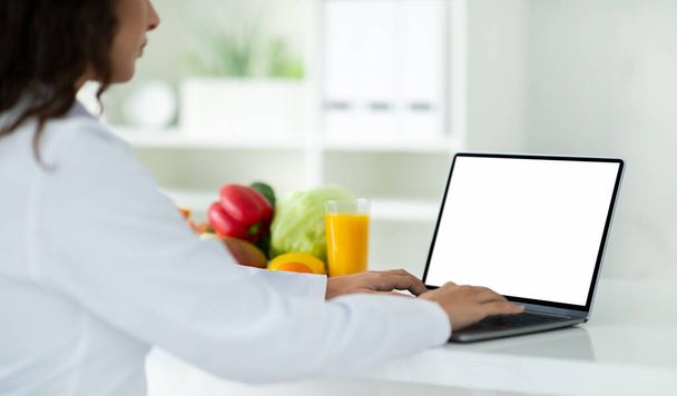 Über-die-Schulter-Ansicht eines Ernährungswissenschaftlers mit Laptop, der Patienten online in der Klinik berät, am Schreibtisch sitzt und Gewichtsabnahme im Web berät, Computer mit weißem leeren Bildschirm, Leerraum - Foto, Bild