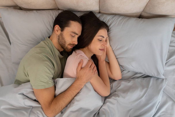 Contenuti giovane coppia in un caldo abbraccio, sdraiato vicino a letto, con espressioni di pace e intimità, suggerendo comfort e affetto - Foto, immagini