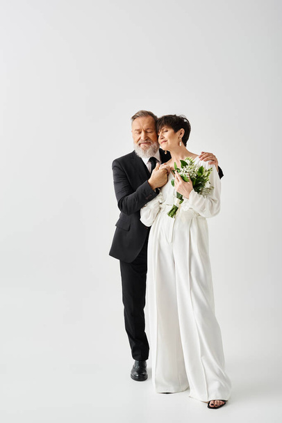 Braut und Bräutigam mittleren Alters in Brautkleidern posieren an ihrem besonderen Tag anmutig zusammen in einem Studio-Setting. - Foto, Bild