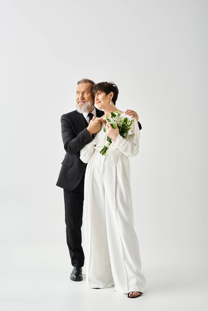 Μεσήλικη νύφη και γαμπρός με νυφικό ντύσιμο ποζάρουν παθιασμένα, ακτινοβολώντας χαρά και αγάπη σε ένα στούντιο. - Φωτογραφία, εικόνα