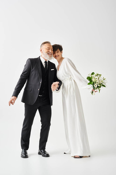 Noiva e noivo de meia-idade, vestidos com vestidos de casamento, fazem uma pose em um estúdio para capturar seu dia especial. - Foto, Imagem