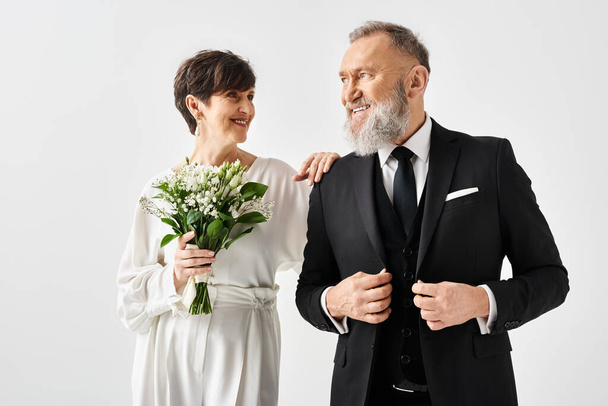 Een bruid en bruidegom van middelbare leeftijd vieren hun speciale dag in een studio, de man in smoking en de vrouw in een witte jurk. - Foto, afbeelding