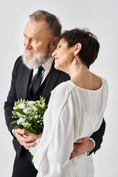 結婚式の服装の中年の花嫁と新郎は一緒に彼らの特別な日を祝うスタジオの設定で喜んで抱きしめます. - 写真・画像