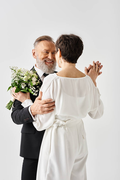 Ein Mann mittleren Alters im Smoking in einer warmen Umarmung mit einer Frau im weißen Hochzeitskleid, die ihren besonderen Tag feiert. - Foto, Bild