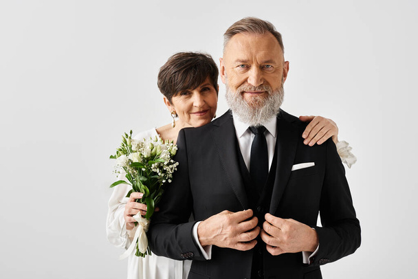 Bruid en bruidegom van middelbare leeftijd in zwart-wit trouwkleding vieren hun speciale dag in een studio-setting. - Foto, afbeelding