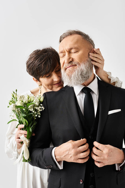 Noiva de meia-idade e noivo em trajes de casamento elegantes abraçar uns aos outros em seu dia especial em um estúdio. - Foto, Imagem