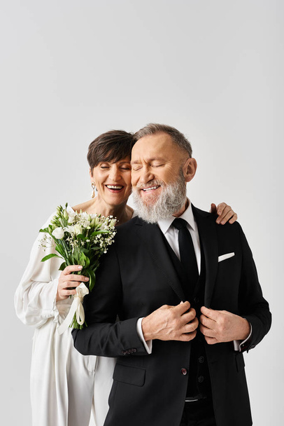 A middle-aged bride and groom in wedding gowns joyfully hugging each other, celebrating their special day in a studio setting. - Photo, Image