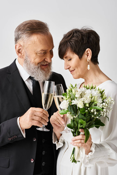 Panna młoda i pan młody w średnim wieku w stroju ślubnym, z wdziękiem trzymający kieliszki szampana w radosnej uroczystości. - Zdjęcie, obraz