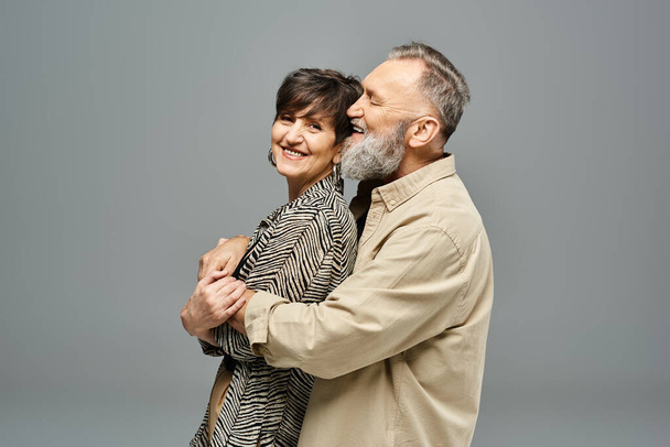 Mężczyzna i kobieta w średnim wieku w stylowym stroju dzielą ciepły uścisk w studio. - Zdjęcie, obraz
