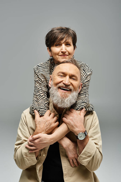 Ein Mann mittleren Alters hält eine Frau auf seinen Schultern in einem stilvollen Studio-Setting. - Foto, Bild