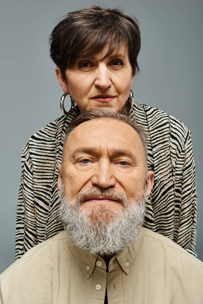 Een man met een baard in stijlvolle kleding staat vooraan, terwijl een vrouw achterin kijkt met een mysterieuze uitdrukking. - Foto, afbeelding