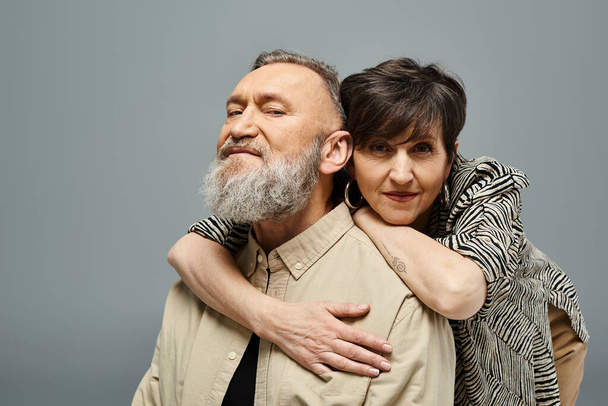 Un hombre de mediana edad con barba abraza tiernamente a una mujer con un atuendo elegante en un entorno de estudio. - Foto, Imagen