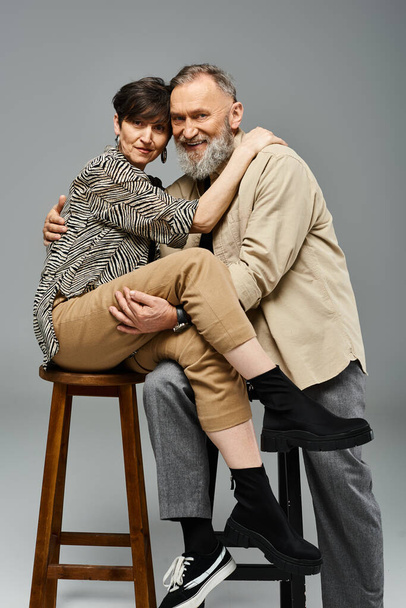 Mężczyzna i kobieta w średnim wieku w stylowym stroju siedzący na stołku w studio. - Zdjęcie, obraz