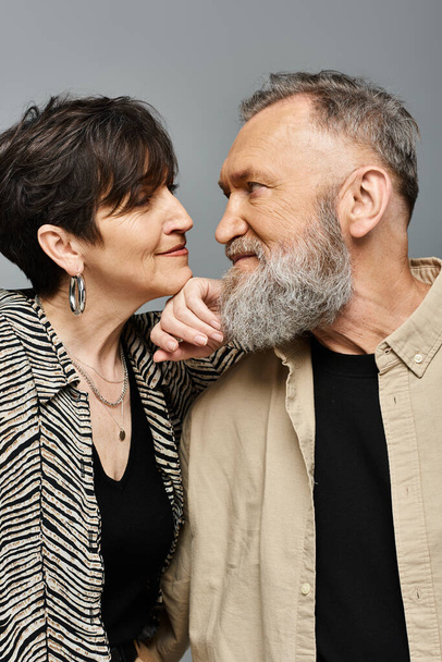 Ein Mann und eine Frau mittleren Alters stehen Seite an Seite in stilvoller Kleidung und verströmen Raffinesse und Anmut in einem Studio-Setting. - Foto, Bild