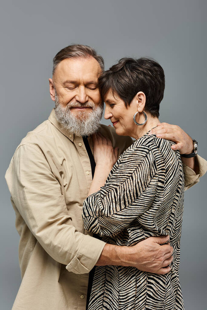 Ένας μεσήλικας άντρας και μια γυναίκα με στυλάτη ενδυμασία αγκαλιάζονται σφιχτά σε ένα στούντιο, εκφράζοντας αγάπη και σύνδεση. - Φωτογραφία, εικόνα