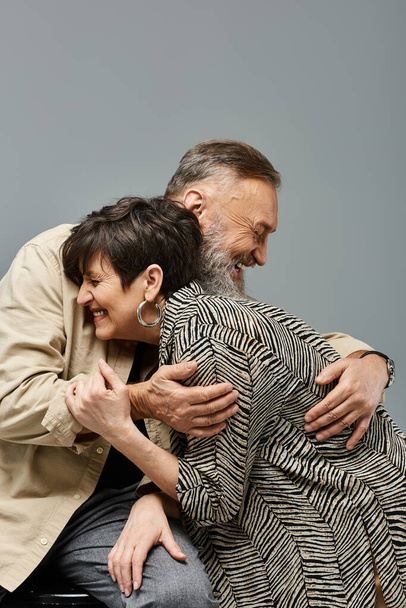 Un homme d'âge moyen étreint amoureusement une femme par derrière sur le dossier d'une chaise dans un cadre de studio élégant. - Photo, image