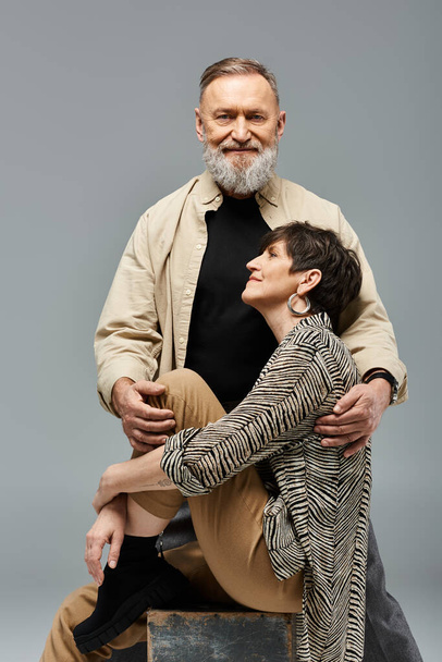 Keski-ikäinen mies istuu voitokkaasti naisen päällä tyylikkäässä puvussa studioympäristössä.. - Valokuva, kuva