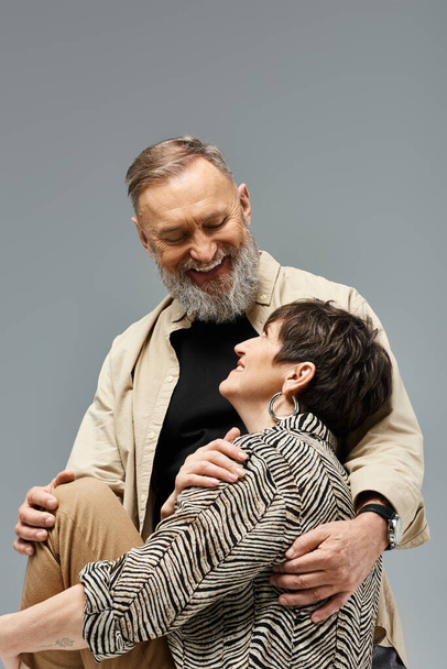 Un hombre y una mujer de mediana edad con un atuendo elegante que comparten un cálido abrazo en un entorno de estudio. - Foto, Imagen