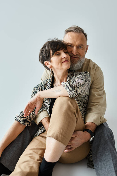 Stylish middle-aged couple seated closely, exuding charm and sophistication in a studio setting. - Photo, Image