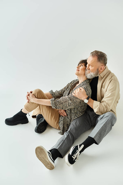 Un hombre y una mujer de mediana edad con un atuendo elegante sentados juntos en el suelo en una pose serena. - Foto, imagen