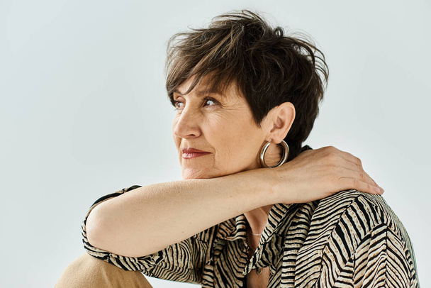 A middle aged woman with short hair sits gracefully on a chair in a studio setting, exuding style and sophistication. - Photo, Image