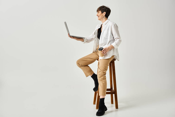 Een man van middelbare leeftijd met kort haar zit op een kruk terwijl hij een laptop vasthoudt in een studio.. - Foto, afbeelding