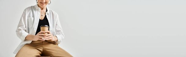 Жінка середнього віку з коротким волоссям у стильному одязі, сидячи на табуреті, загорнута в її мобільний телефон. - Фото, зображення