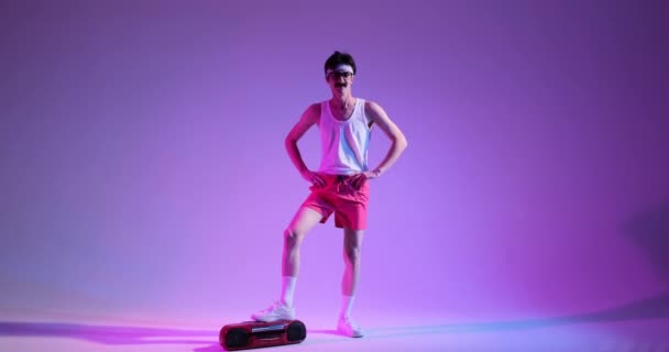 Fröhlicher kaukasischer junger Mann mit Schnurrbart tanzt und hört Musik, steht neben Kassettenspieler über lila Hintergrund im Neonlicht. - Filmmaterial, Video