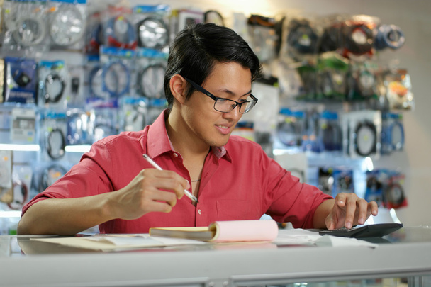 Китаец, работающий в компьютерном магазине, проверяет счета и счета
 - Фото, изображение
