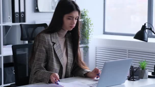 Gestresste en ernstige Kaukasische jonge vrouw werkt met documenten en laptop in een moderne kantooromgeving. Haast maken voor de deadline. - Video