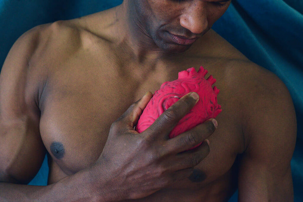 романтическая посадка молодой африканский черный мускулистый мужчина держит объект в форме сердца изображают эмоции и любят высокий имидж - Фото, изображение