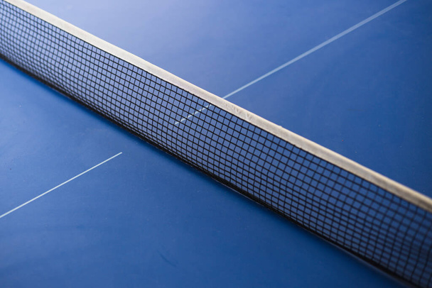 Großaufnahme eines Netzes auf blauem Tisch für Tischtennis. Das Konzept von Sport und gesundem Lebensstil. - Foto, Bild
