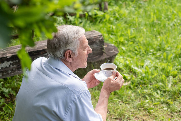 Starší muž usrkává čaj se zaměřením na relaxaci a jednoduchost vychutnávání přírody, ideální pro volný čas a odchod do důchodu, seniorské pojetí pojištění. Kvalitní fotografie - Fotografie, Obrázek