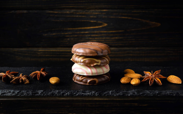 Μια στοίβα σοκολατένια μπισκότα ή σοκολατένια μπράουνι με ξηρούς καρπούς και αστεροειδή γλυκάνισο σε μαύρο πίνακα σερβιρίσματος. Νόστιμο επιδόρπιο έννοια για πρωινό. - Φωτογραφία, εικόνα