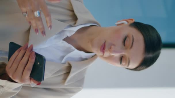 Χαρούμενη γυναίκα που μιλάει σε βιντεοκλήση χρησιμοποιώντας ασύρματα ακουστικά στο δρόμο από κοντά. Ευτυχισμένη νεαρή κοπέλα κάνει online συνέδριο με φίλους στο smartphone κάθετα βίντεο. Χαμογελαστή κοπέλα που κοιτάζει οθόνη. - Πλάνα, βίντεο
