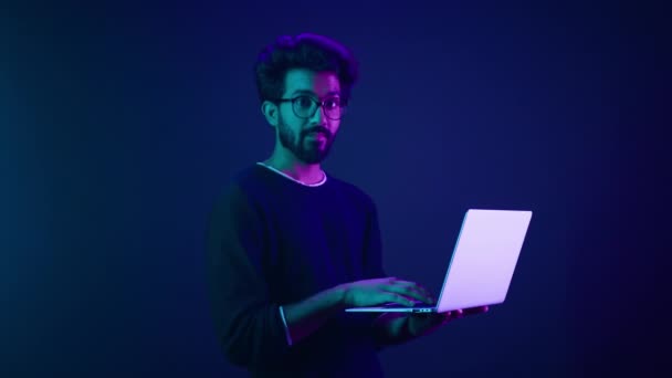 Arabisch indiaan man man man man man programmeur programmeur internet computer ontwikkelaar zakenman man gamer houden laptop computer uit te nodigen hier welkom knik hoofd uitnodiging werk in violet neon achtergrond - Video