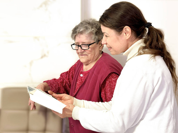 Vapaaehtoinen sosiaalityöntekijä jakaa tietonsa iäkkään naisen kanssa samalla kun selittää kirjan sisältöä. Empatian, myötätunnon, heikkojen auttamisen käsite - Valokuva, kuva