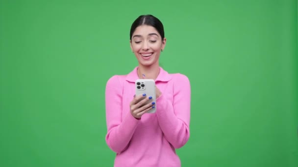 Portret van een blanke positieve, vrolijke vrouw met behulp van mobiele telefoon, chatten in social media app, surfen op internet op groene achtergrond. - Video