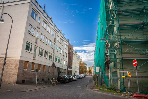 ケルンに駐車された複数の物語の建物や車を持つ典型的なドイツの住宅街. 建物改修プロジェクトの建設現場が右側に見える. - 写真・画像