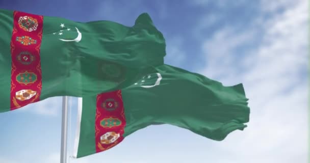 Türkmenisztán nemzeti zászlók lobognak egy tiszta napon. Zöld mező, vörös függőleges sáv, félhold, öt csillag, szőnyegmotívumok. Zökkenőmentes 3D render animáció. Lassan mozgó hurok. Szelektív fókusz - Felvétel, videó