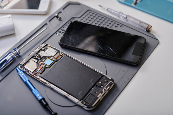 Dva chybně fungující smartphony umístěné na stole profesionálního opraváře spolu s pracovními nástroji - Fotografie, Obrázek