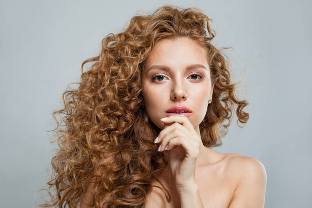Θετική κοκκινομάλλα θηλυκό μοντέλο με μακριά κατσαρά μαλλιά τζίντζερ και καθαρό μαλακό φρέσκο δέρμα ποζάροντας σε λευκό φόντο. Studio μόδας πορτρέτο ομορφιά της νεαρής γυναίκας - Φωτογραφία, εικόνα